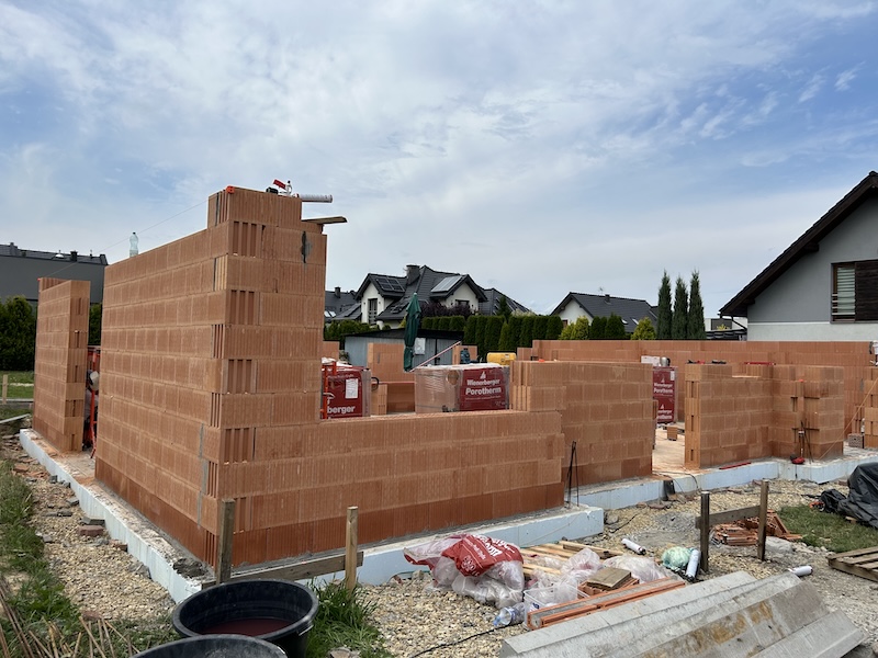 Murowanie ścian domu jednorodzinnego z pustaków ceramicznych Budowa ścian domu jednorodzinnego z pustaków ceramicznych poryzowanych – murarz przy pracy na rusztowaniu