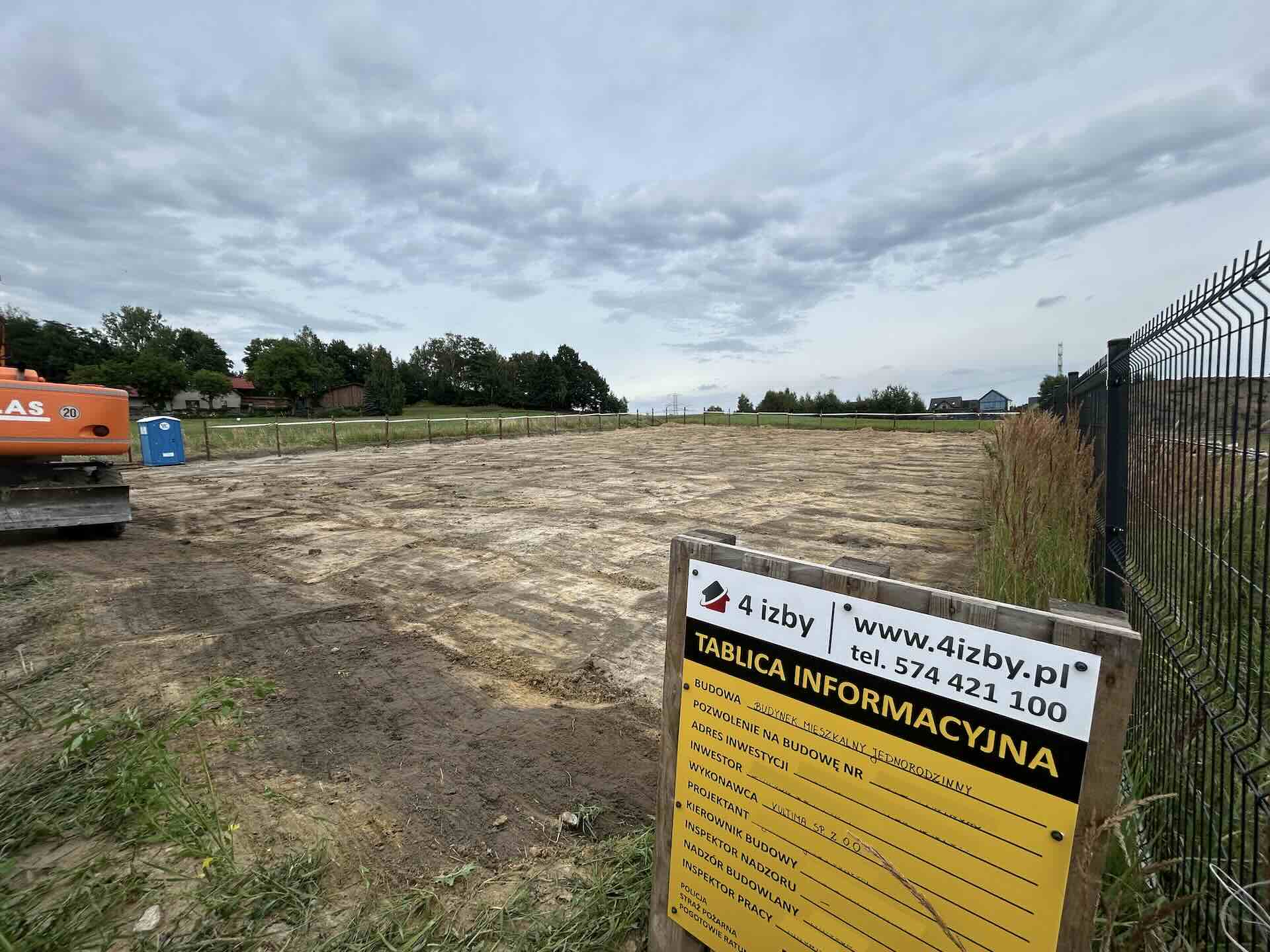 Żółta tablica informacyjna budowy z wymaganymi danymi zamontowana na ogrodzeniu
